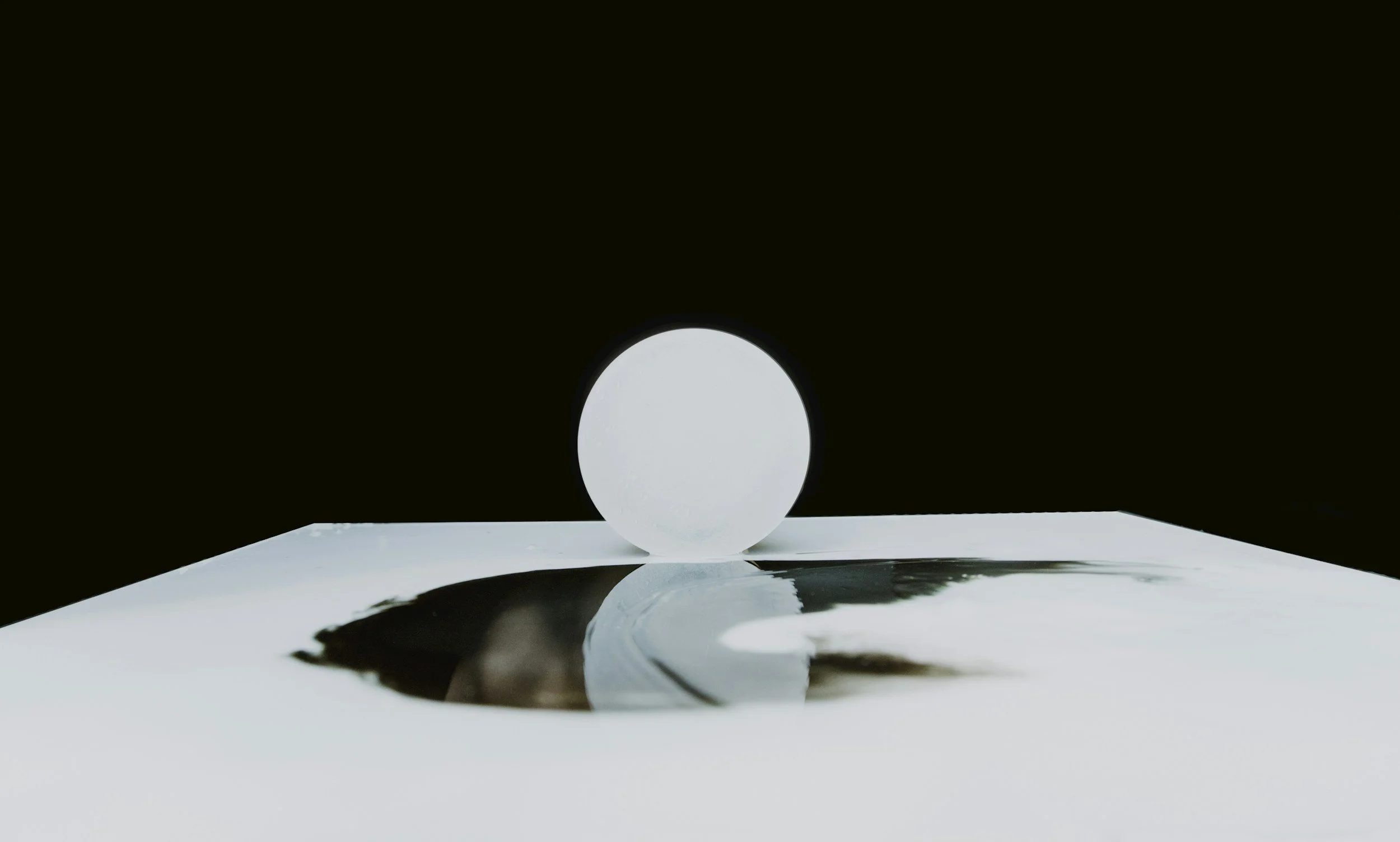 A white sphere resting on a reflective surface with a black background.