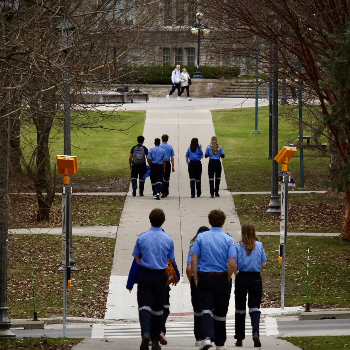 Group of students walking on a college campus sidewalk near trees and streetlights.