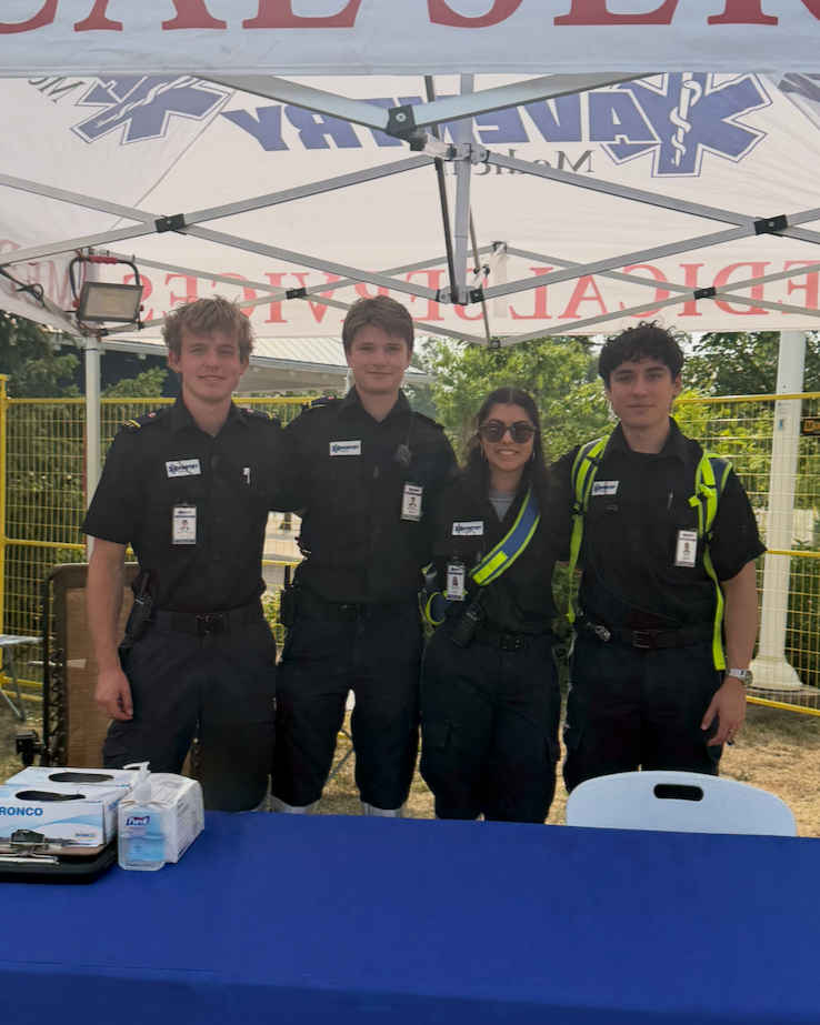 Four Aventry paramedics in uniform standing under a tent at an outdoor event, smiling and posing for the photo.