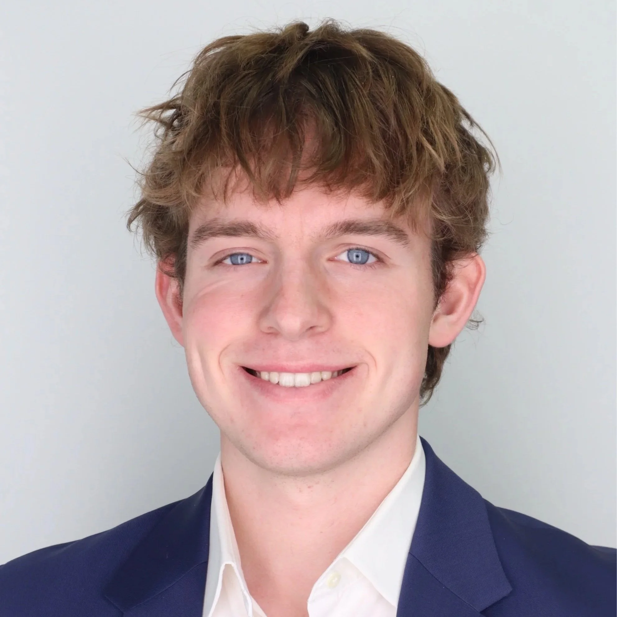 Aventry Medical Co-Founder Ryan Lutz with brown curly hair, blue eyes, smiling, wearing a navy suit and white shirt.