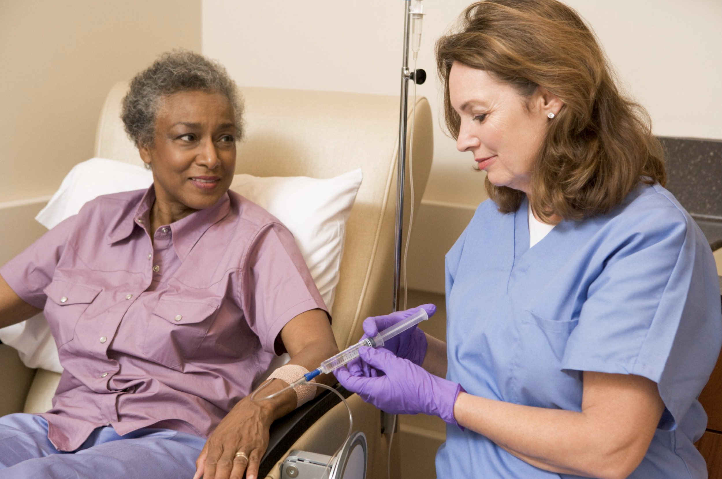A nurse preparing an injection for an elderly female patient lying in a hospital bed.