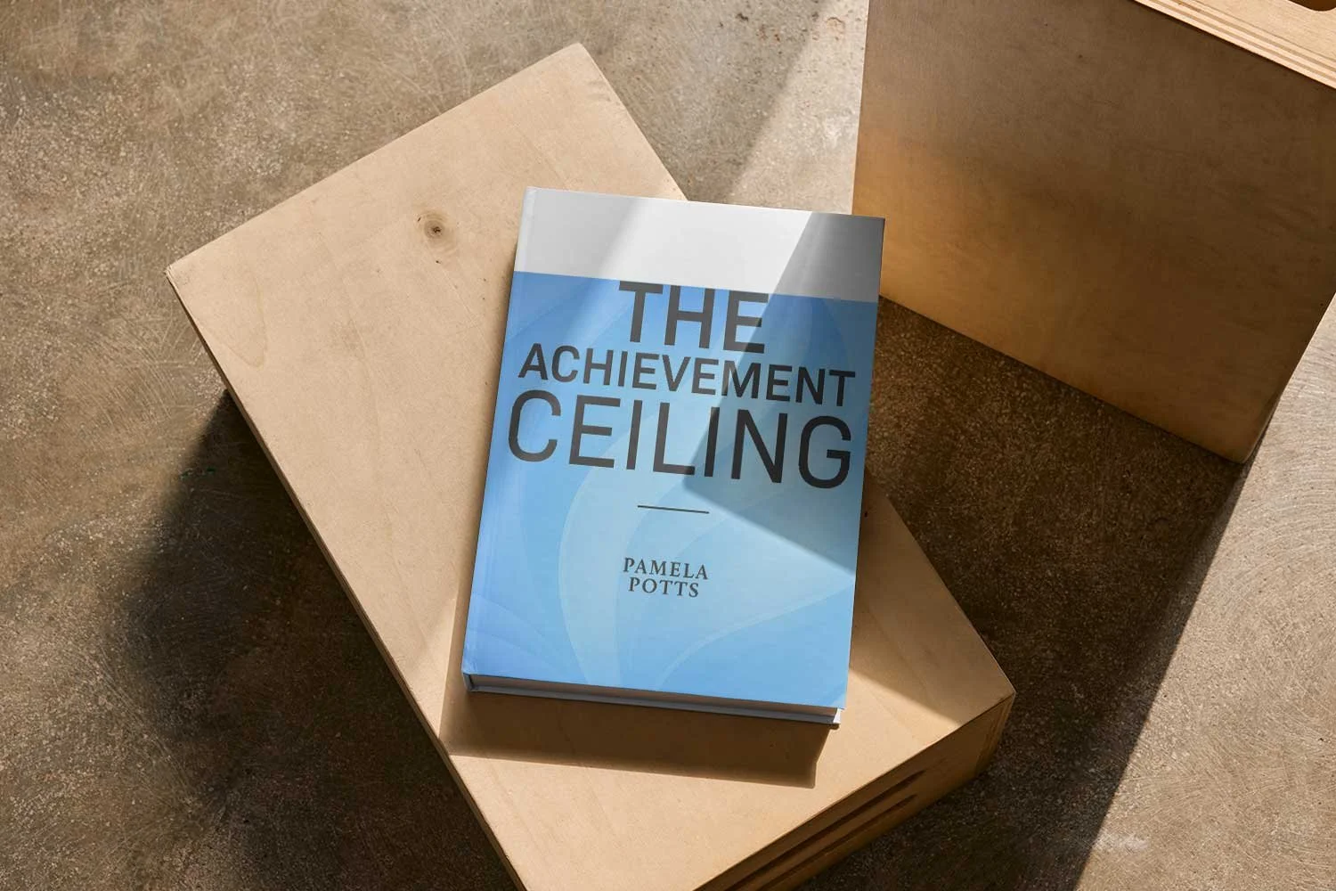 A book titled 'The Achievement Ceiling' by Pamela Potts resting on a light wooden stool, with a darker wooden box in the background and natural sunlight casting shadows on the scene.
