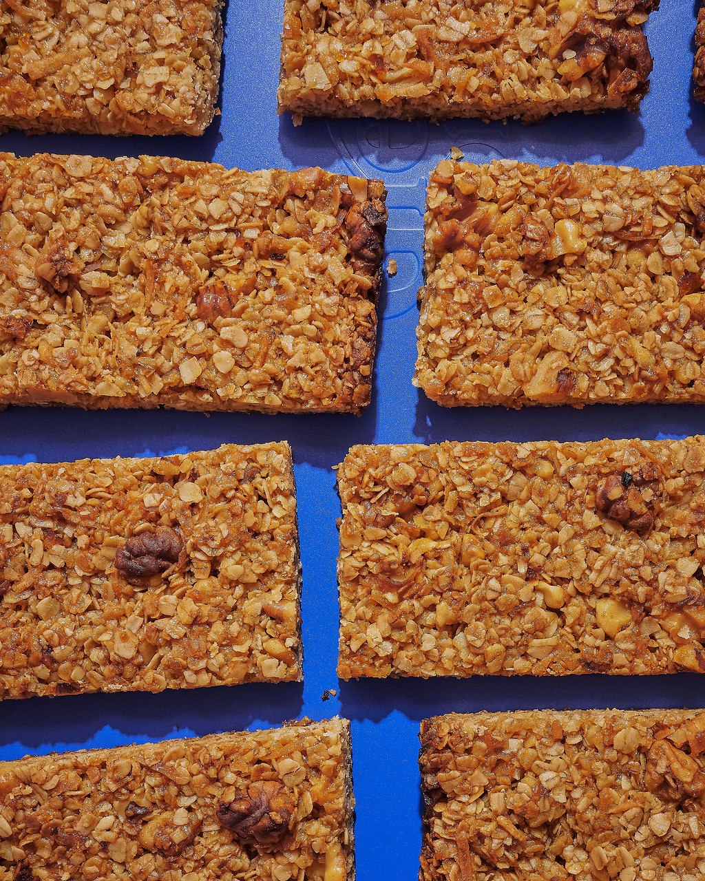 Close-up of multiple rectangular nut and oatmeal bars on a blue surface.