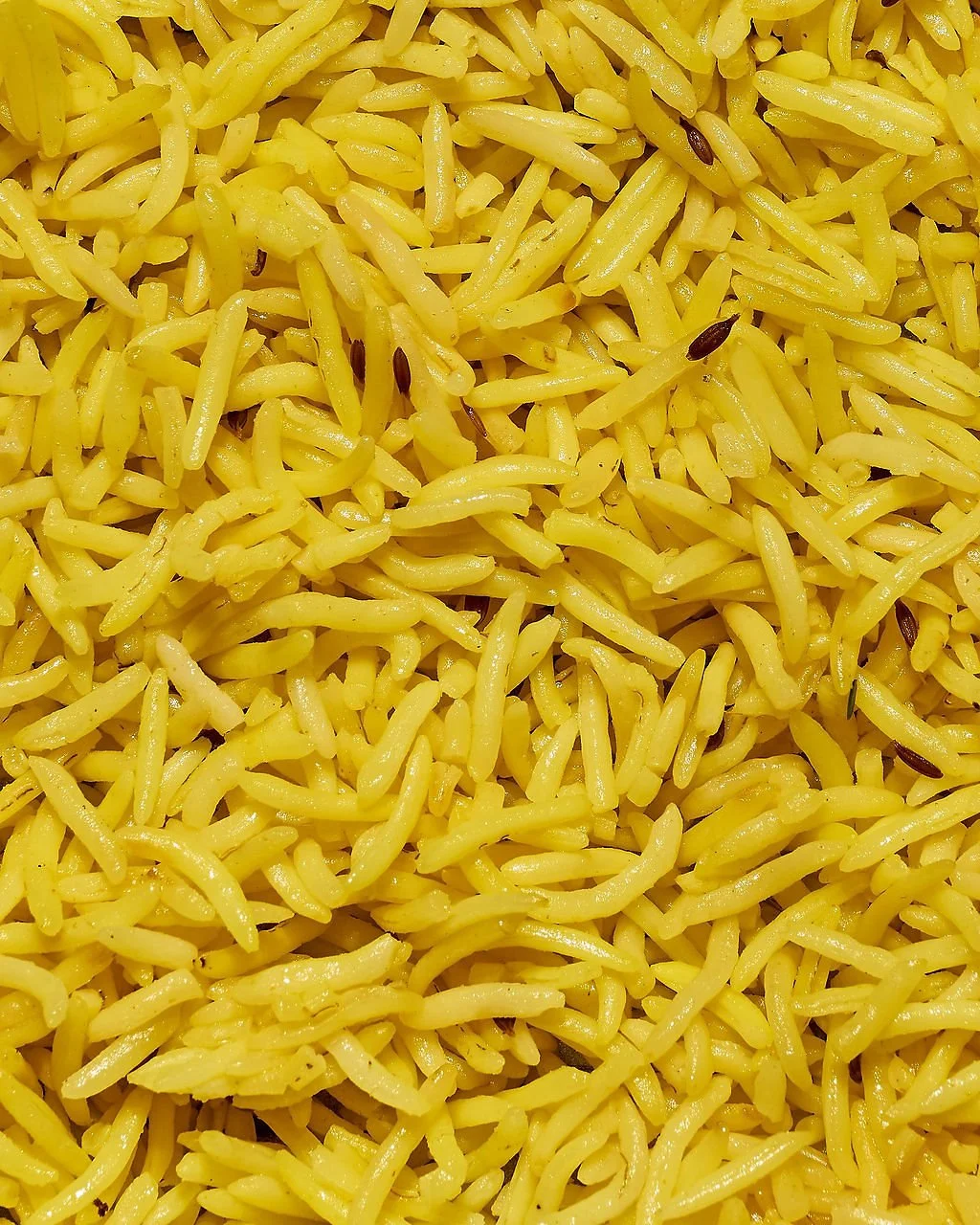 Close-up view of cooked yellow rice with some black cumin seeds.