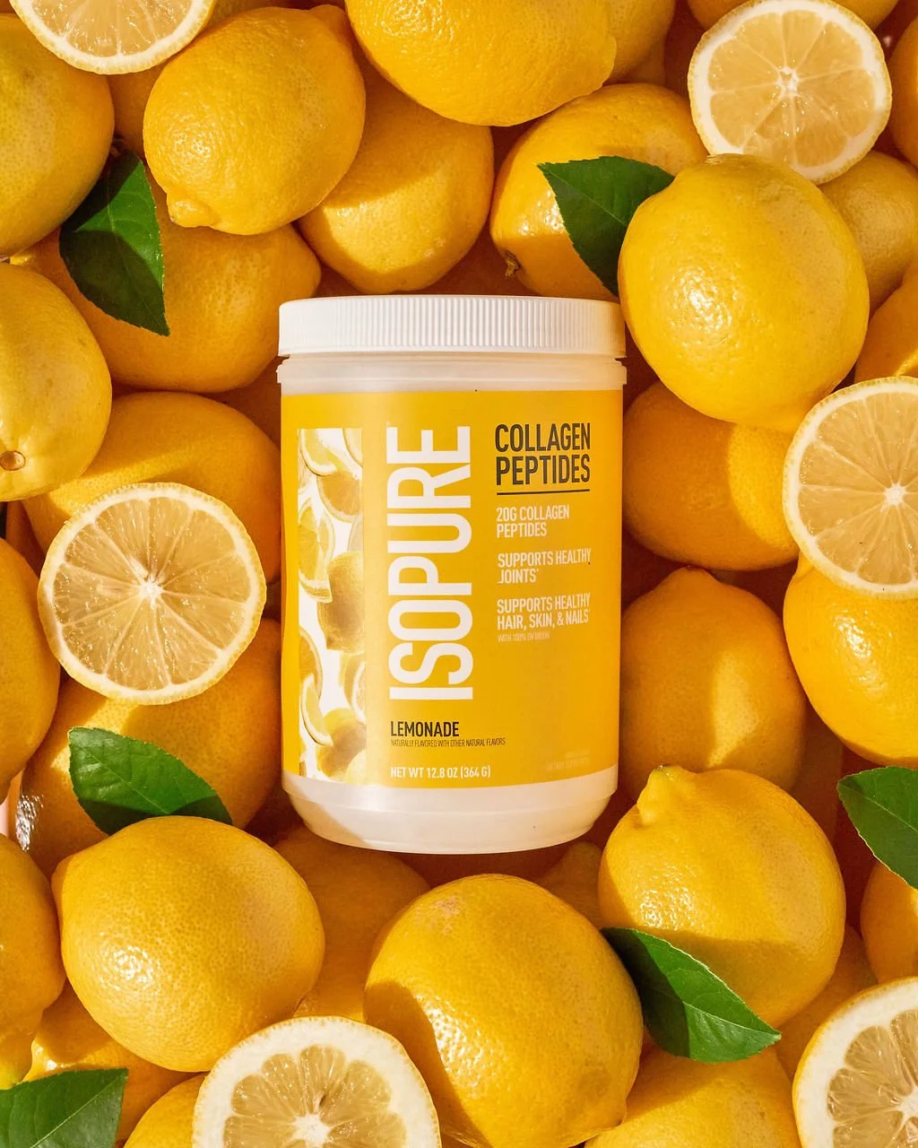 A container of Isopure collagen peptides lemon flavored supplement surrounded by fresh whole and sliced lemons with a few green leaves.