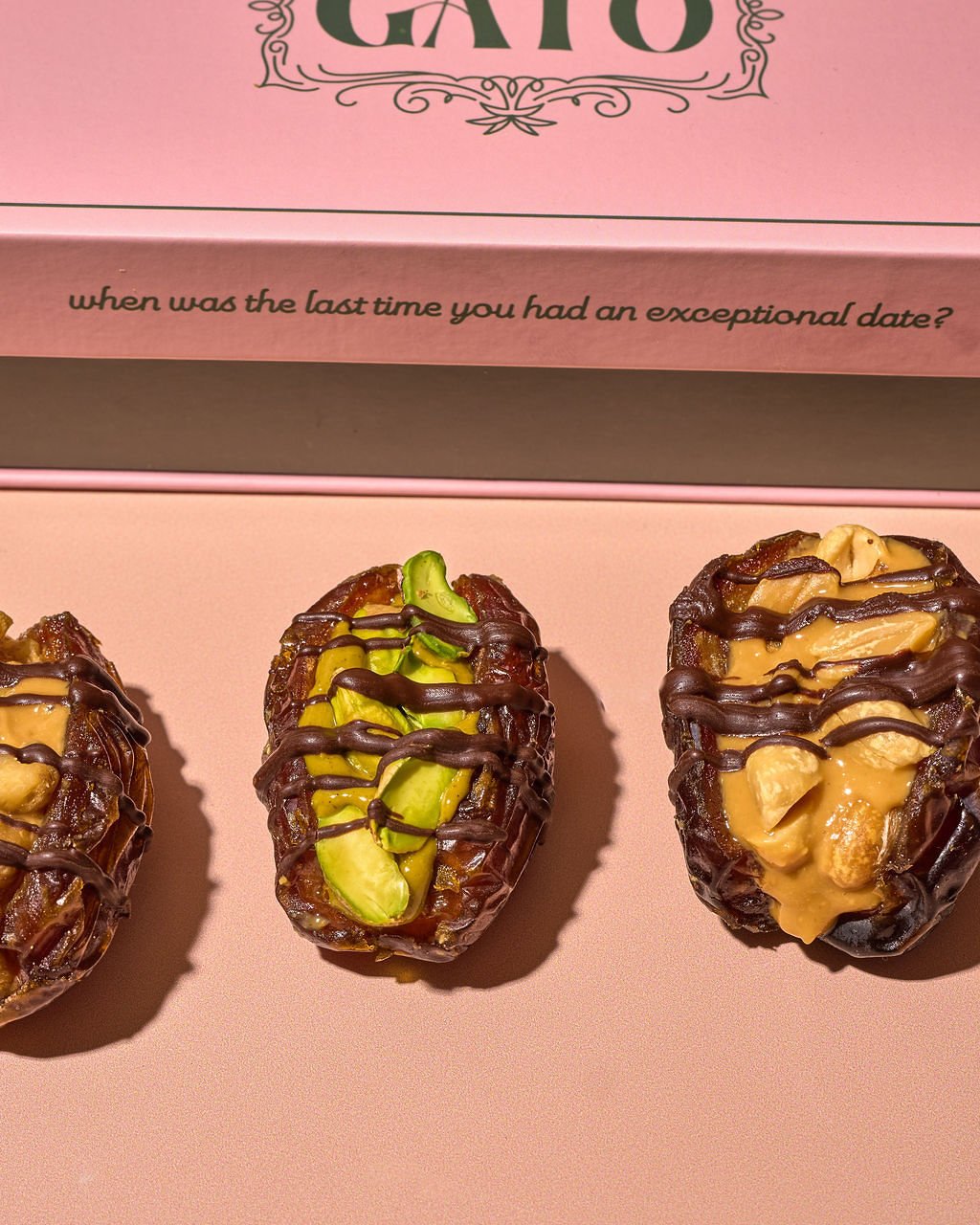 Three date-filled chocolates topped with nuts and drizzled with chocolate, placed on a pink surface