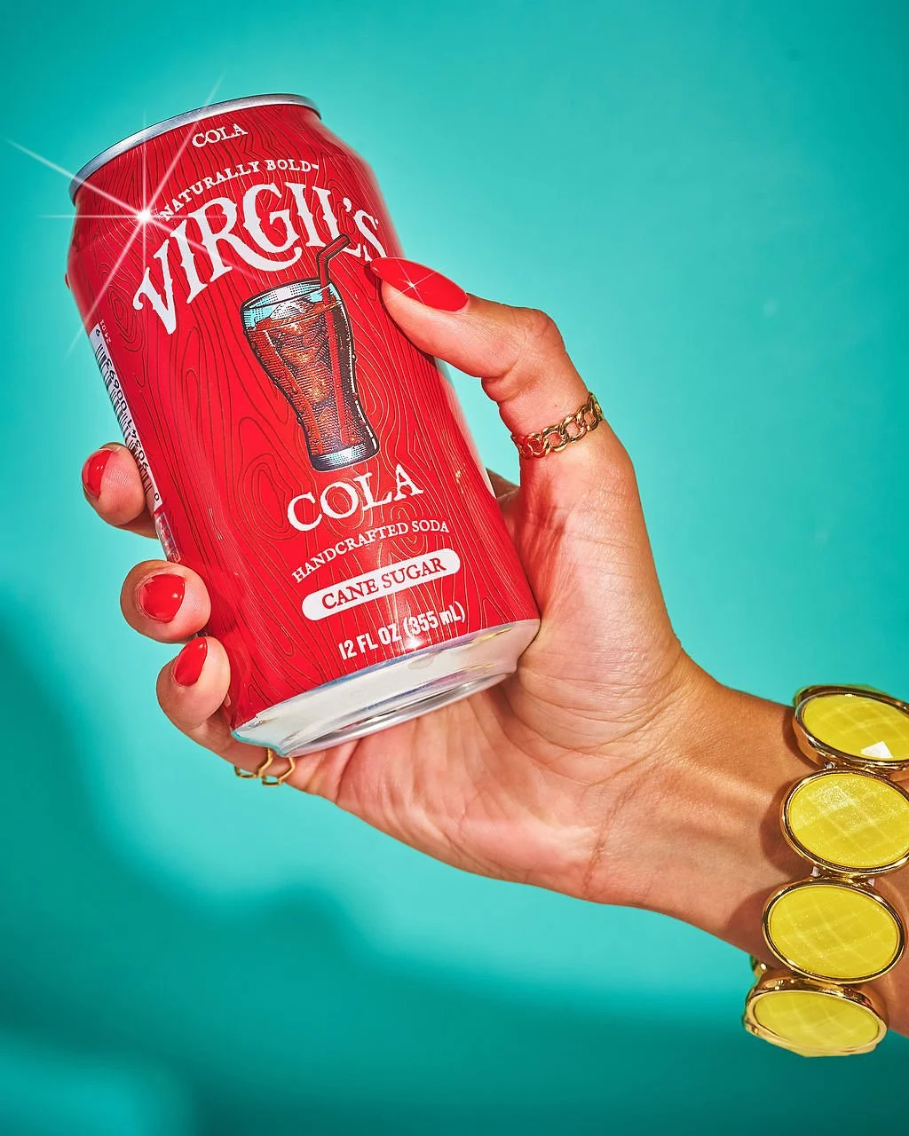 Person holding a red soda can labeled Virginia Cola with a graphic of a glass of cola and straw, against a turquoise background.