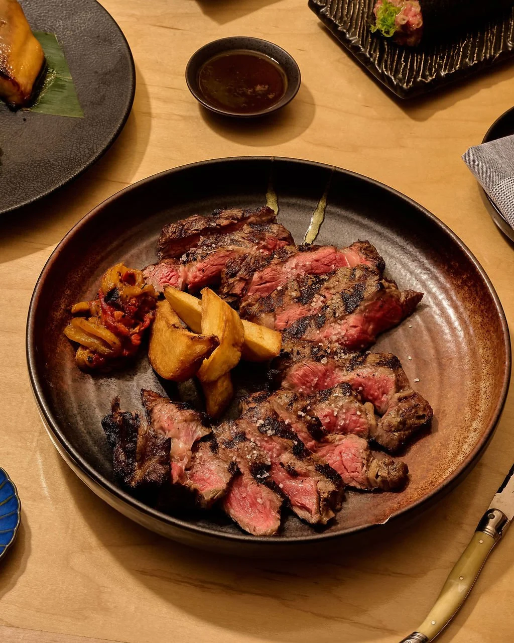 A plate of grilled steak, thick-cut potato wedges, and a side of chopped vegetables.