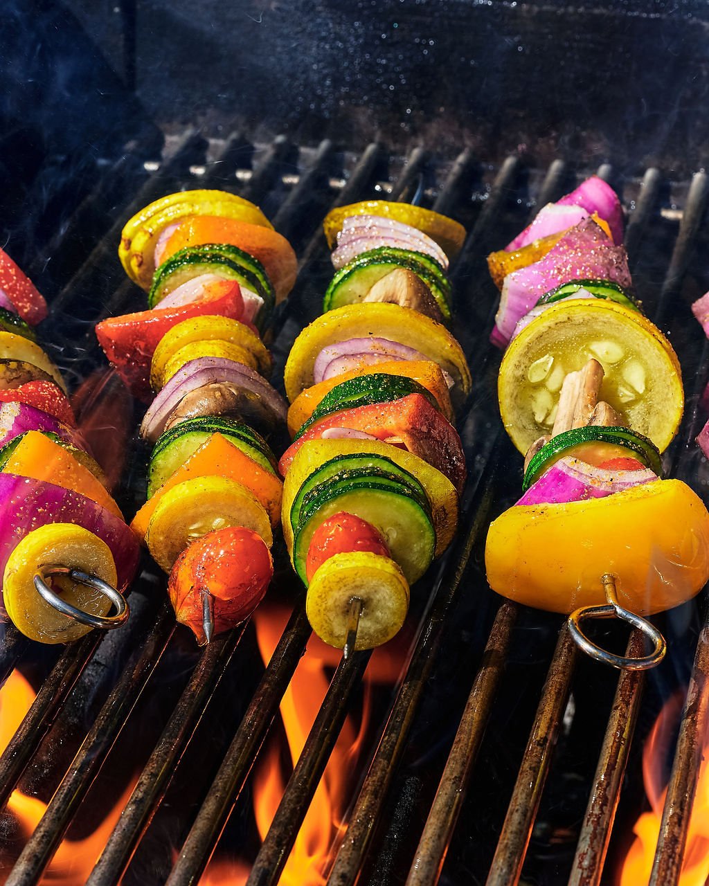 Colorful vegetable skewers grilling over an open flame on a barbecue grill.