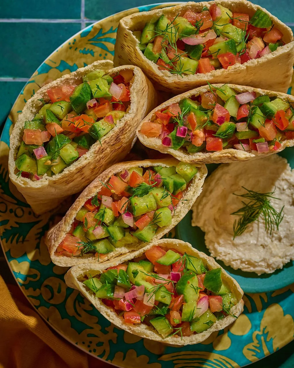 Tacos filled with diced avocado, tomato, red onion, and herbs, served on a decorative plate with a side of white sauce garnished with dill.