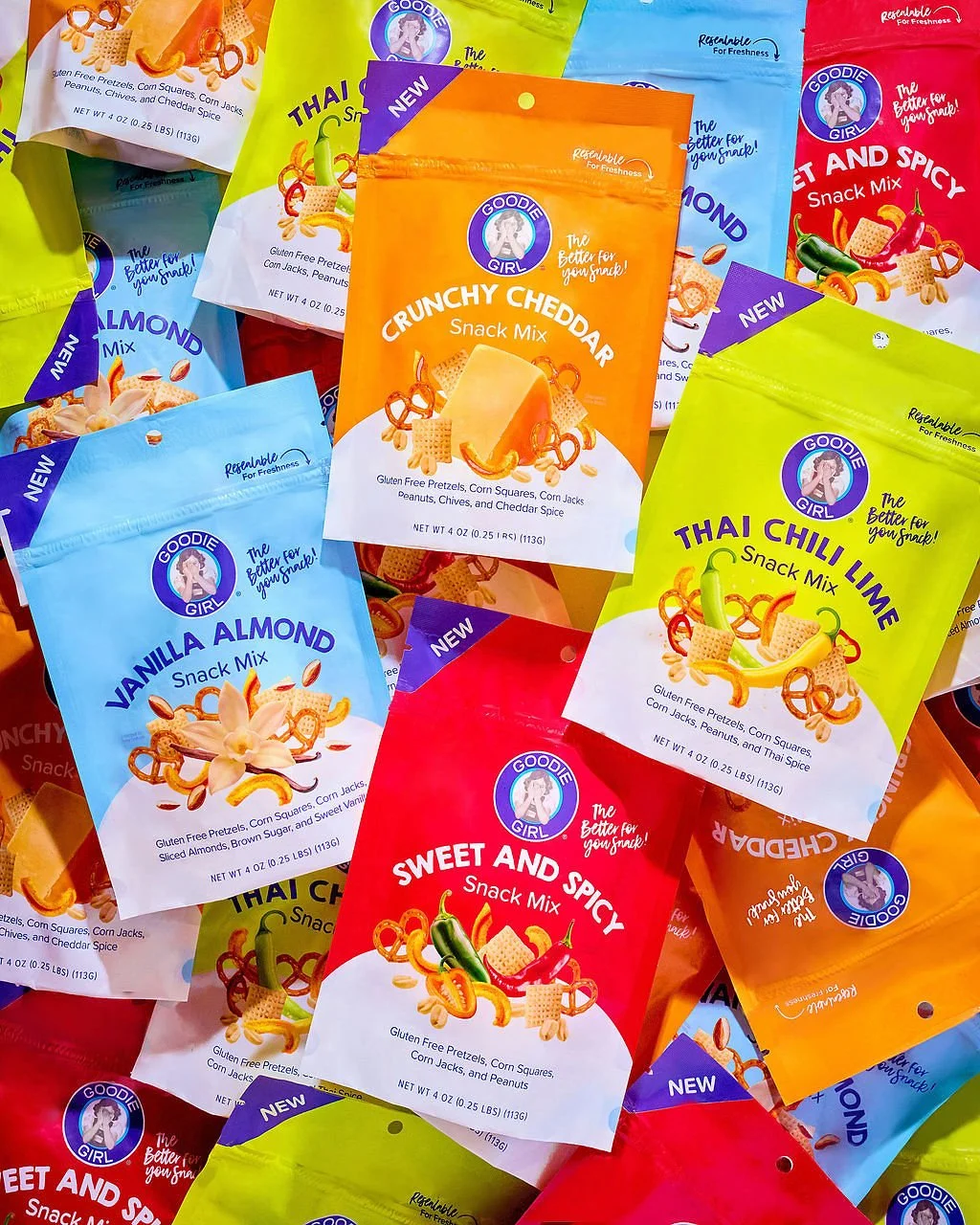 Colorful packets of Goodie Girl snack mixes, including varieties like Crunchy Cheddar, Vanilla Almond, Thai Chili Lime, Sweet and Spicy, and other flavors, spread out in a pile.