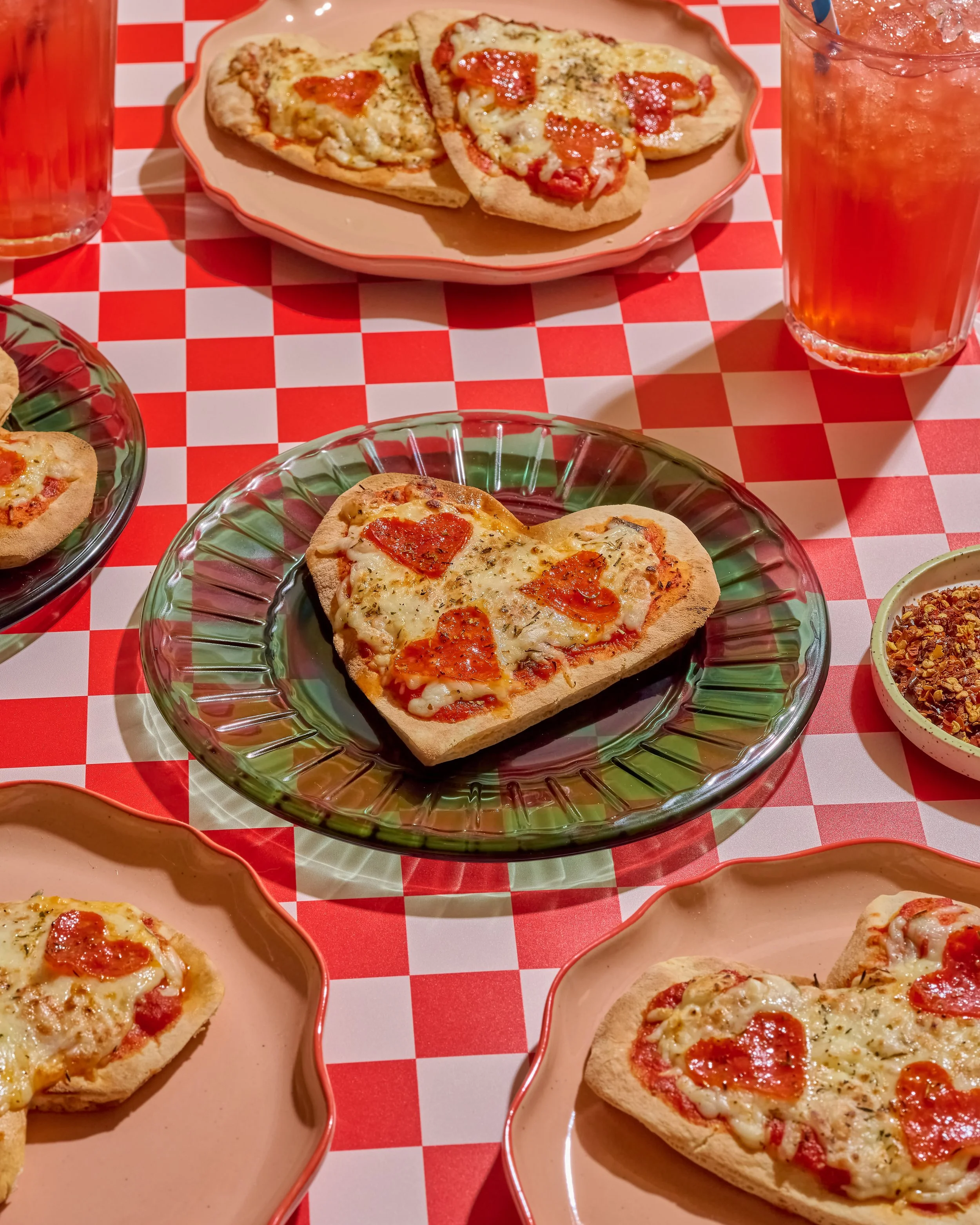 Several slices of pizza with cheese, pepperoni, and tomato on a spotted table with glasses of iced tea.