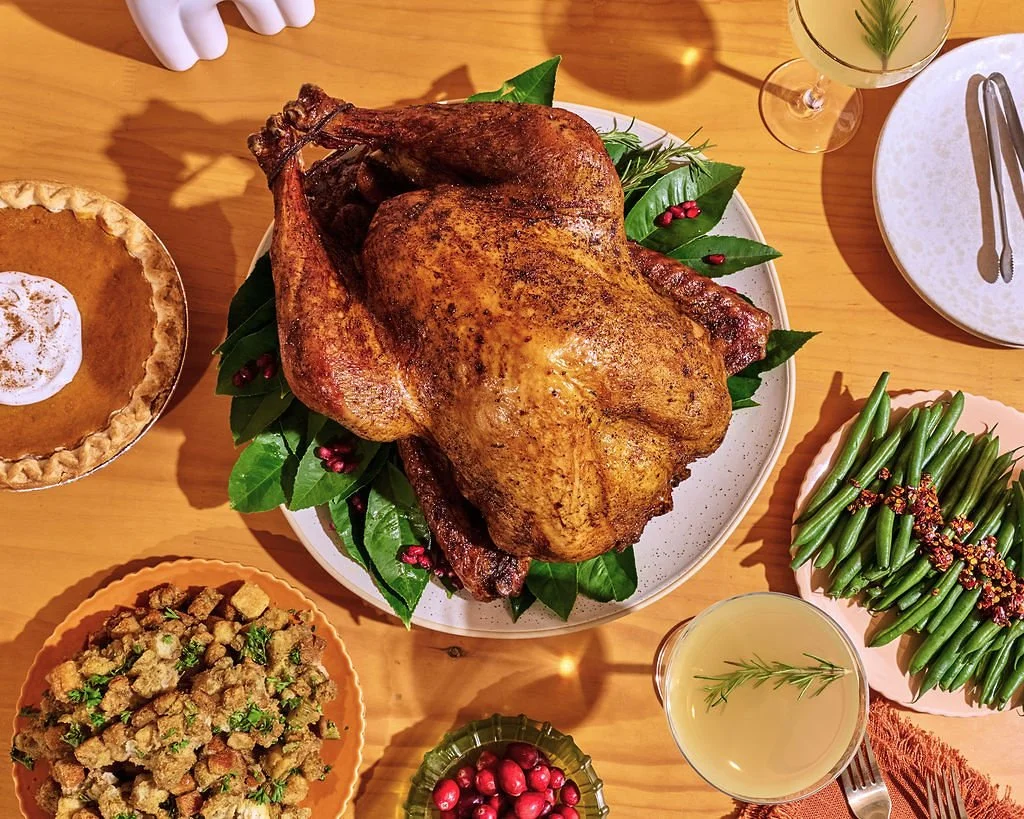 A roasted turkey on a white platter garnished with green leaves and red berries.