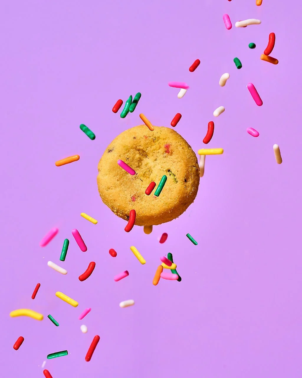 Cookie with colorful sprinkles falling against a purple background.
