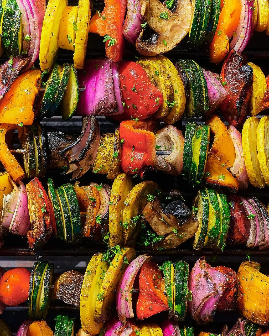 Colorful grilled vegetable skewers with zucchini, yellow squash, red onion, bell peppers, cherry tomatoes, and mushrooms garnished with parsley.