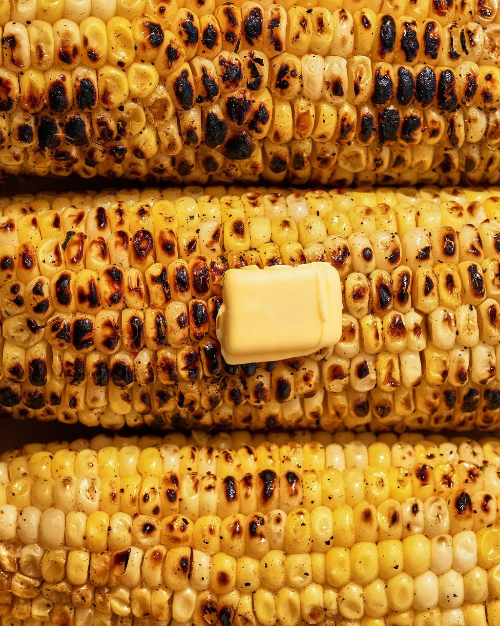 Close-up of grilled corn on the cob with charred kernels and a pat of butter.