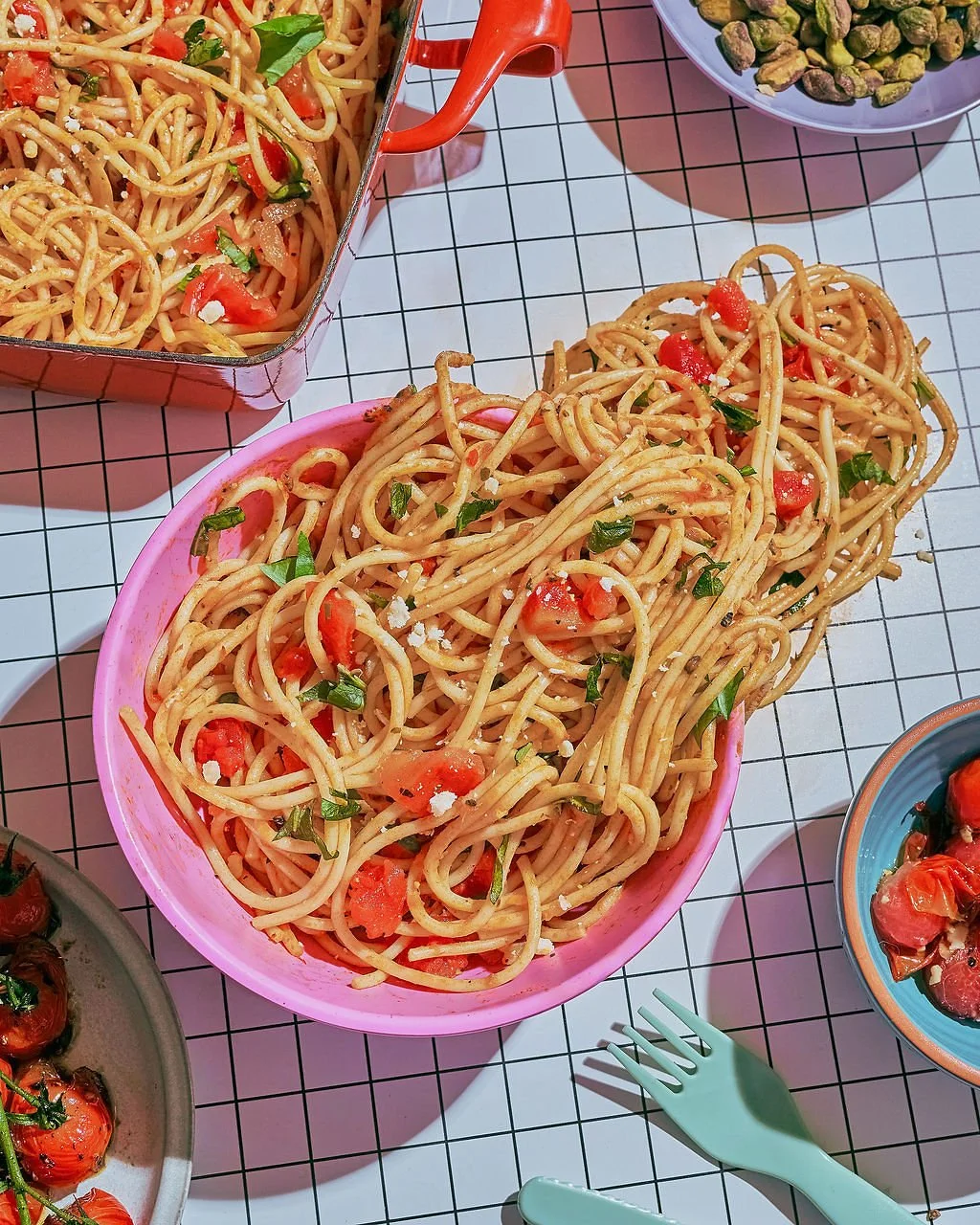 Bowls of spaghetti with tomato, basil, and grated cheese on a grid-patterned table.