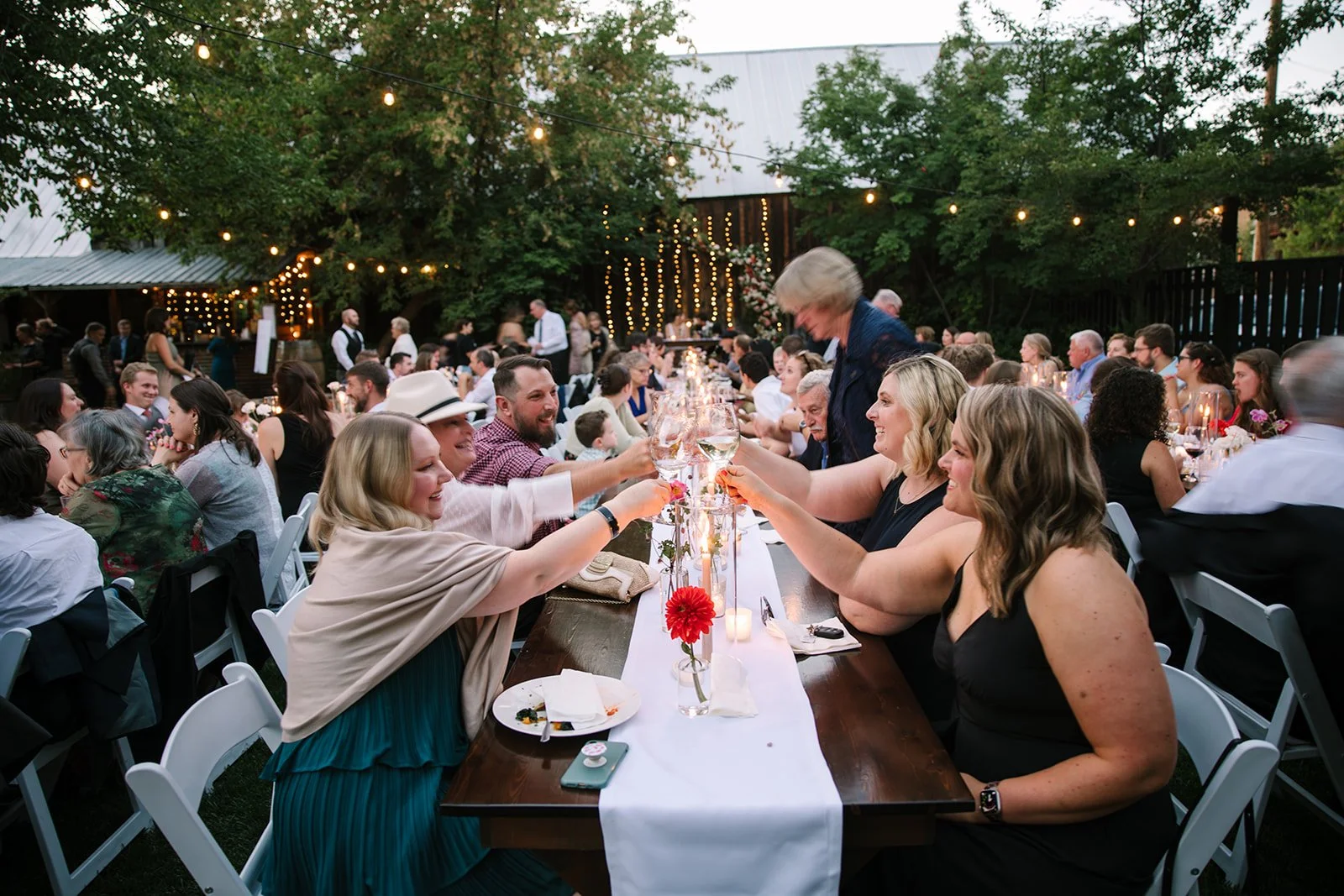 An image of guests giving a "cheers" at an outdoor party at StoneHouse101. StoneHouse101 is an intimate indoor outdoor events venue in Roslyn, Washington, hosting weddings, birthdays, anniversaries, and more near Cle Elum, WA.