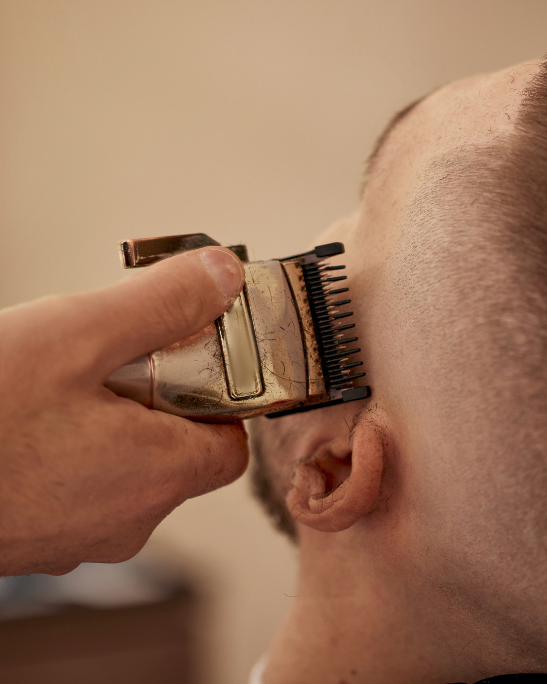 Close-up of a person getting a haircut with an electric hair clipper trimming the side of their head.