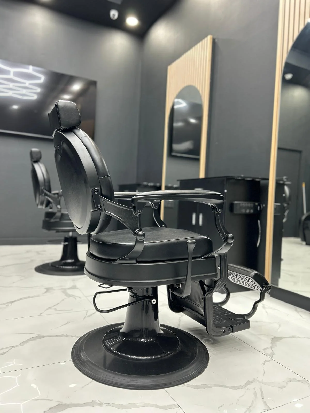 Modern black barber chair with a mirror and flat-screen TV on a black wall in a salon.