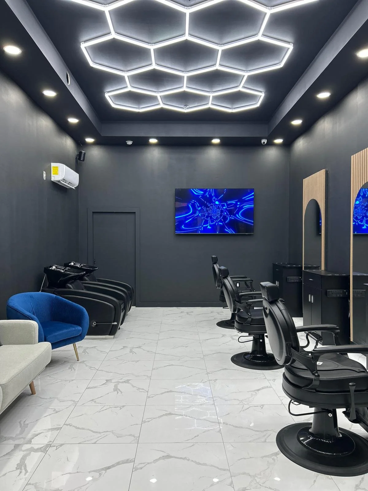 Modern barbershop, Platinum Cuts, with black walls, illuminated ceiling, wall-mounted TV screen, styling chairs, and washing stations with sinks.
