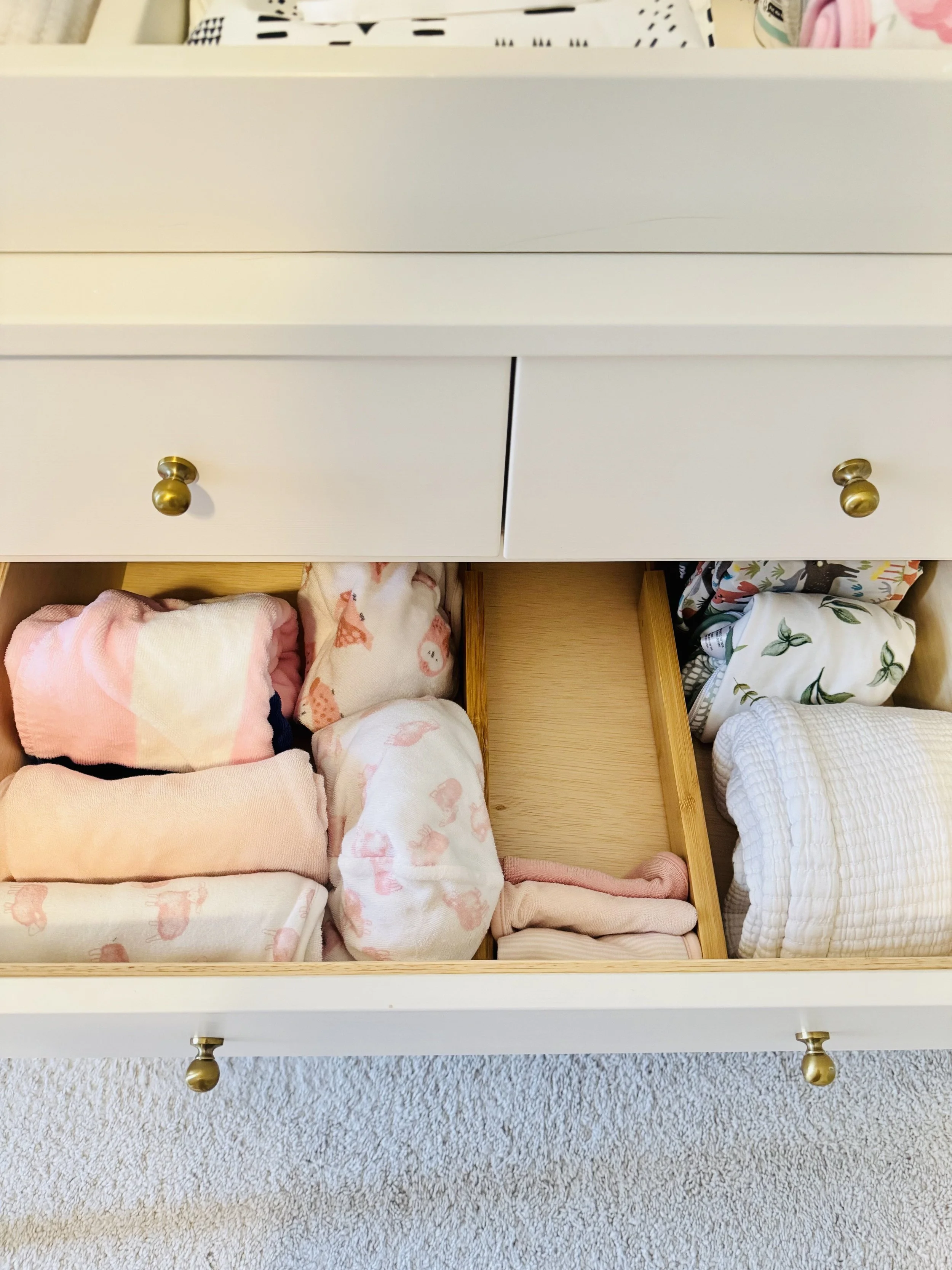 Open drawer in white dresser showing neatly folded baby clothes and blankets inside.
