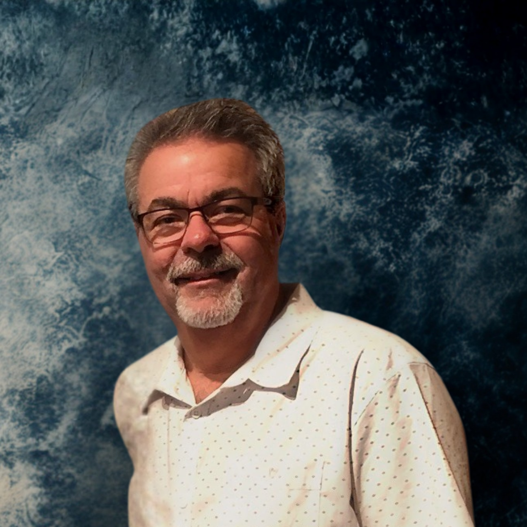 Lyle Chinkin, air quality expert, an older man with glasses and a beard, is smiling while standing in front of a blue abstract background.