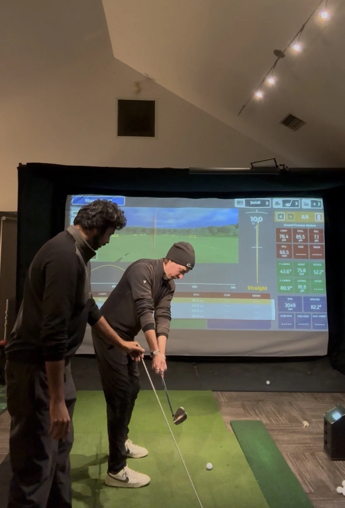Two men playing indoor golf on a simulation screen with a digital golf course background.