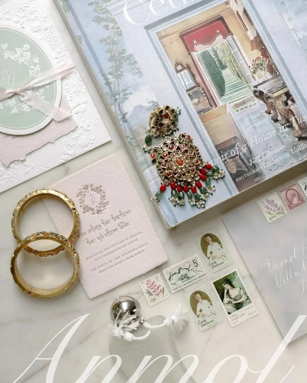 A collection of jewelry, postcards, and decorative items arranged on a white surface, including gold rings, earrings, wedding vows, stamps, and a book with a house interior on the cover.