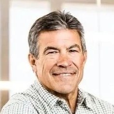 Portrait of a smiling middle-aged man with gray hair wearing a checkered shirt indoors.