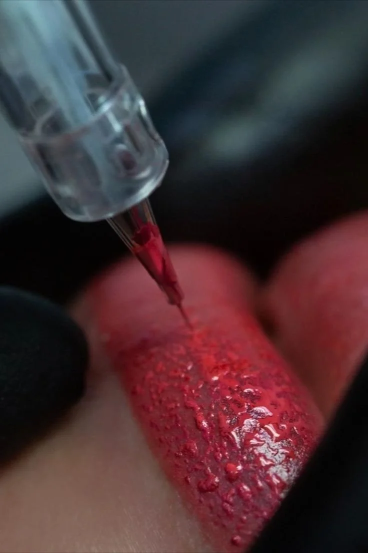 A close-up of a tattooing process with a tattoo machine applying red ink to a person's skin.