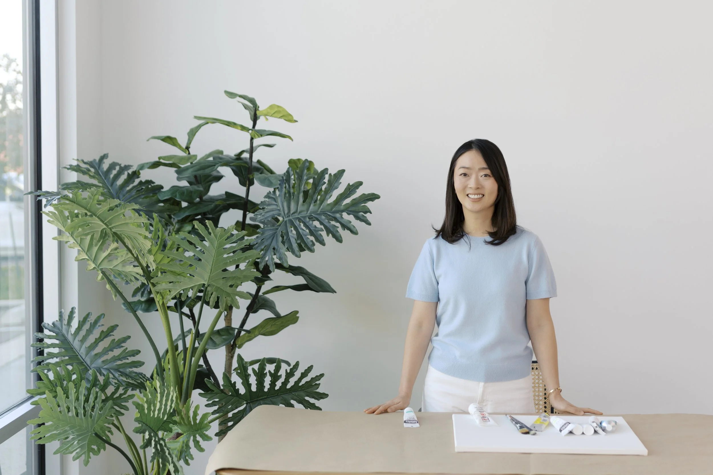 Therapist Juhee surrounded by art supplies, standing behind a canvas and painting during a healing session.