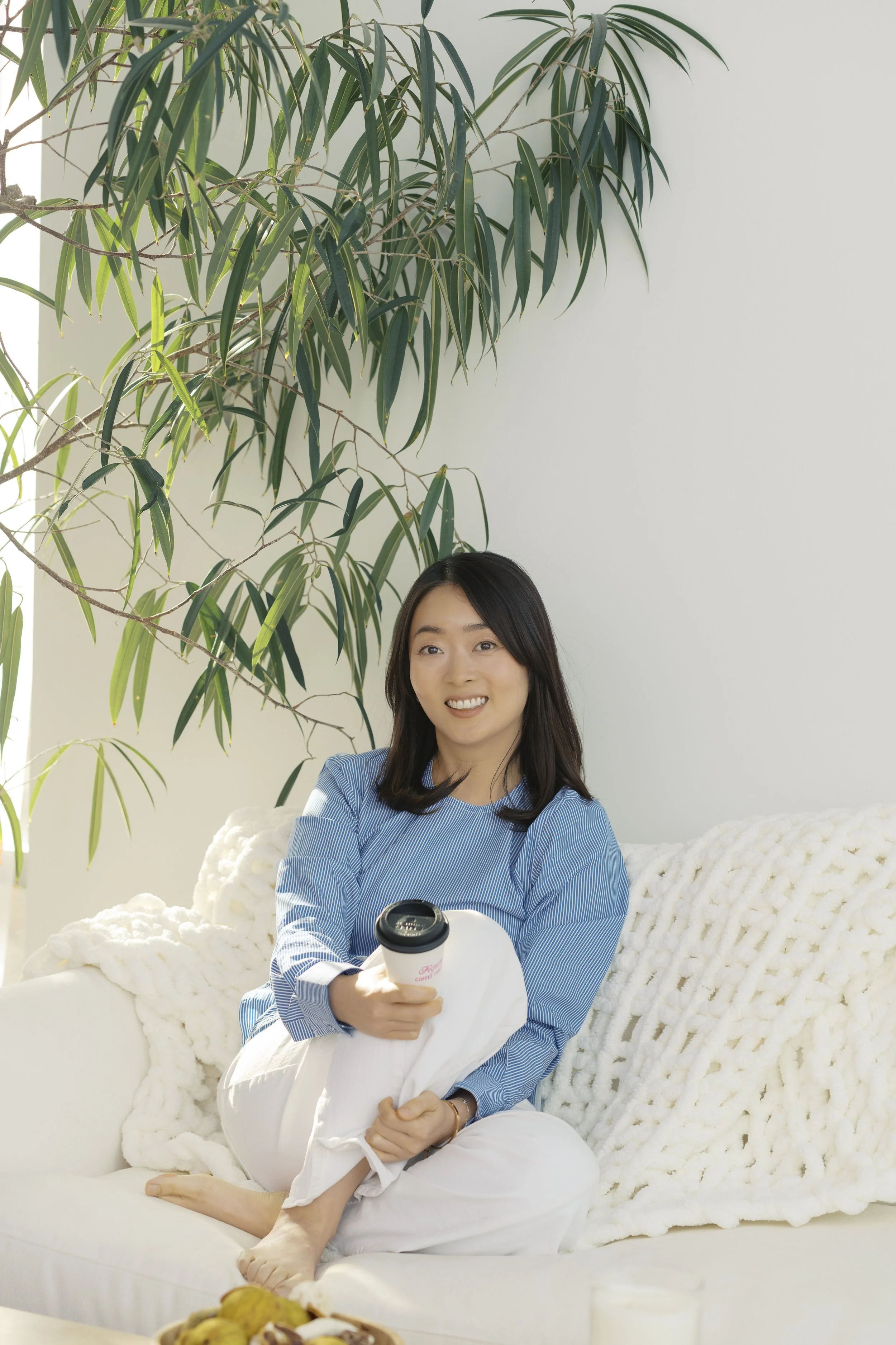 Juhee sitting on a cozy couch, smiling gently during an inner mothering therapy session focused on healing the mother wound.