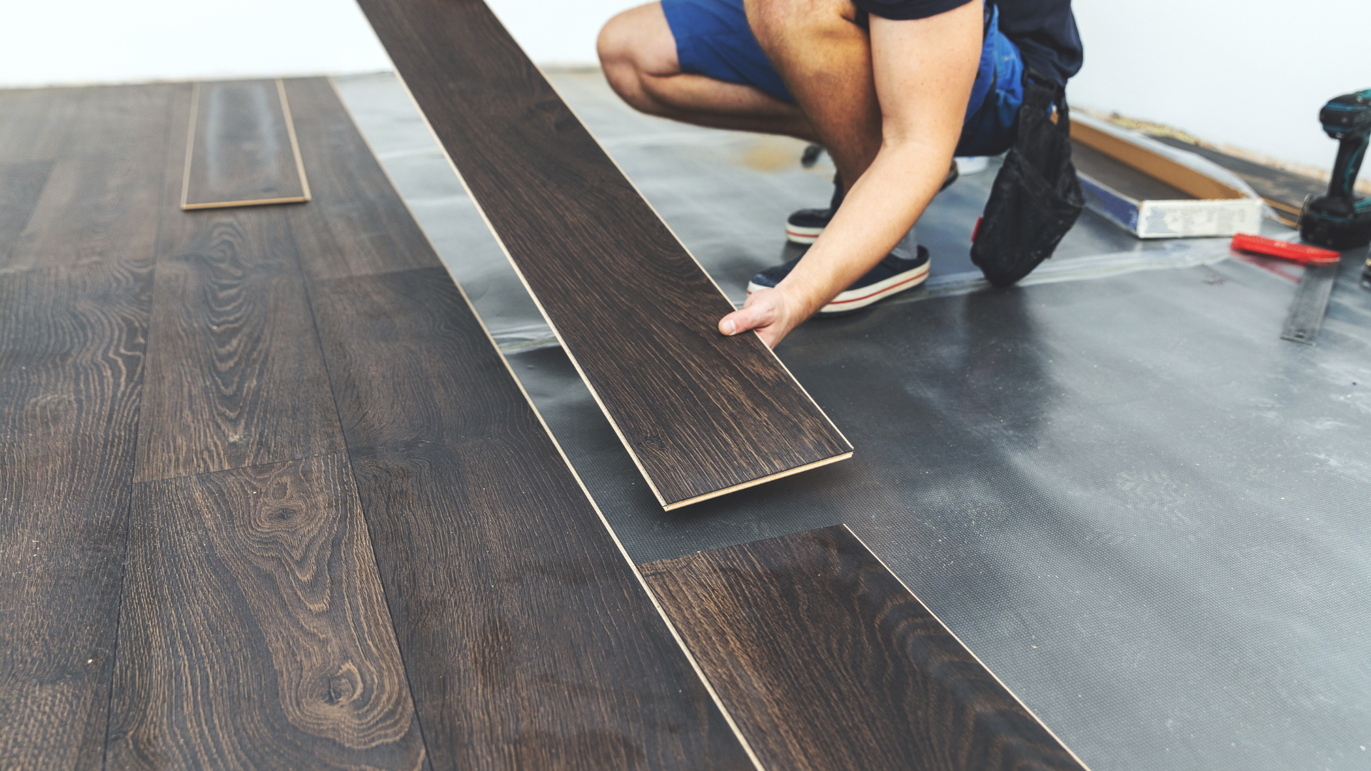Person installing dark wood laminate flooring, fitting planks together on a subfloor.