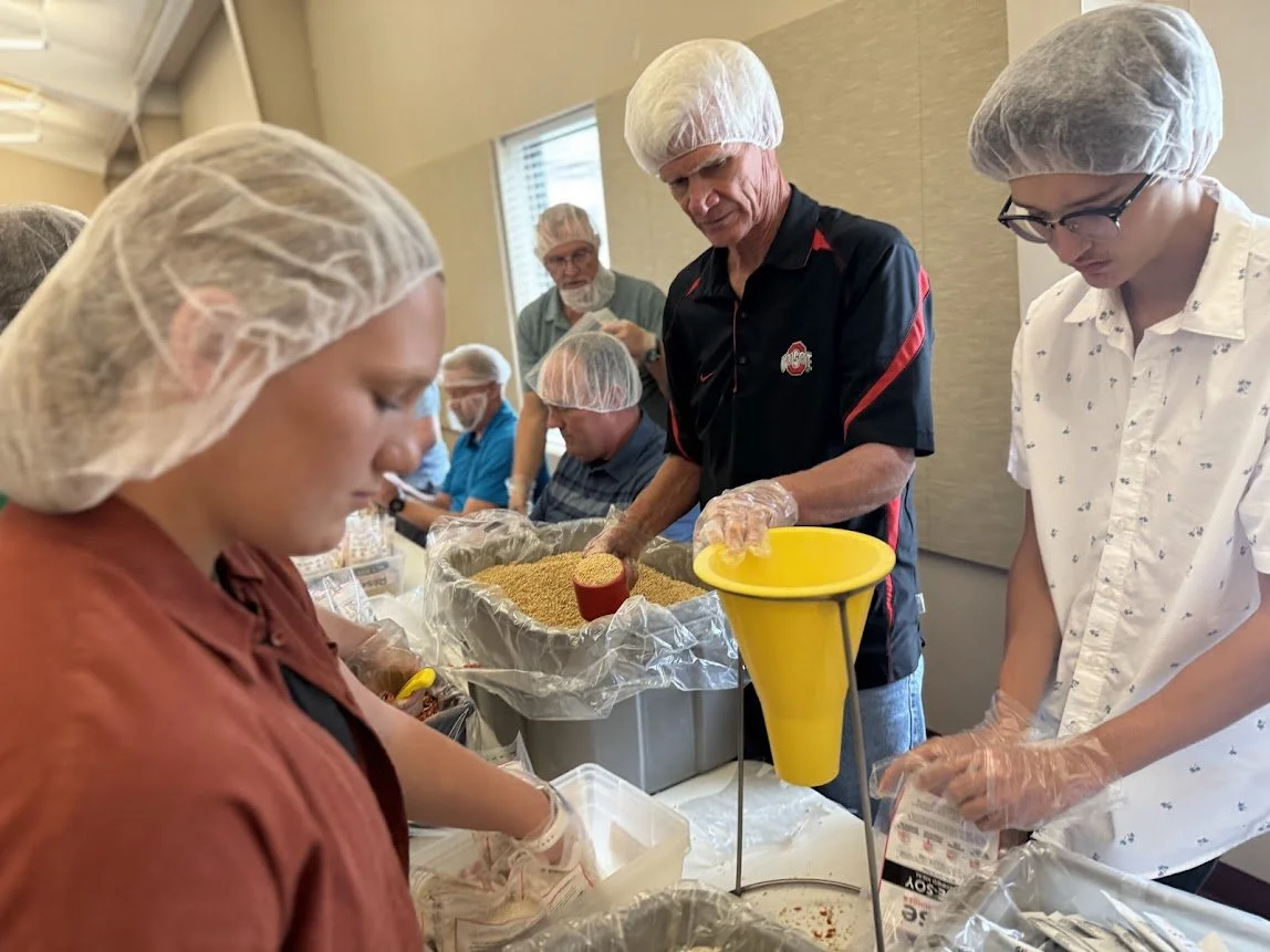 People wearing hairnets and gloves work together filling containers with food ingredients in a room.