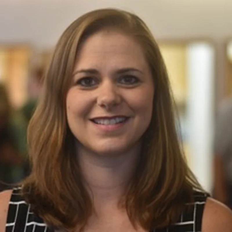 A woman with shoulder-length brown hair smiling at the camera in an indoor setting.