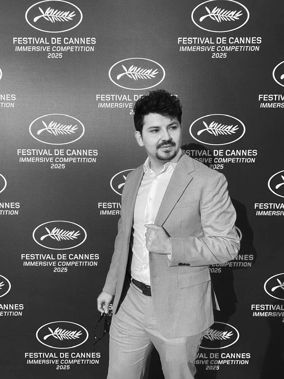 A man in a light-colored suit and white shirt posing in front of a backdrop with the Cannes Film Festival 2025 logo and text.