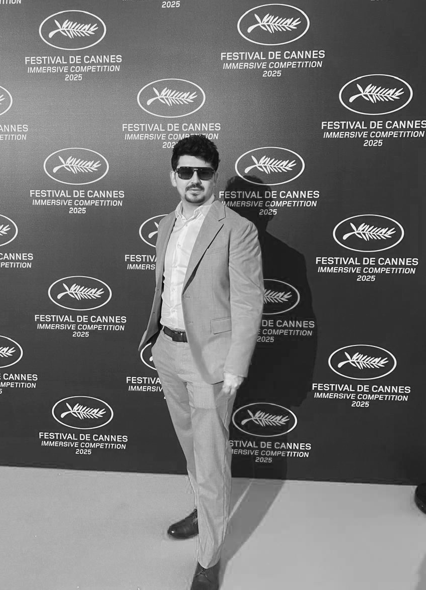 A man in a suit and sunglasses standing in front of a backdrop with logos for the 2025 Cannes Film Festival's immersive competition.