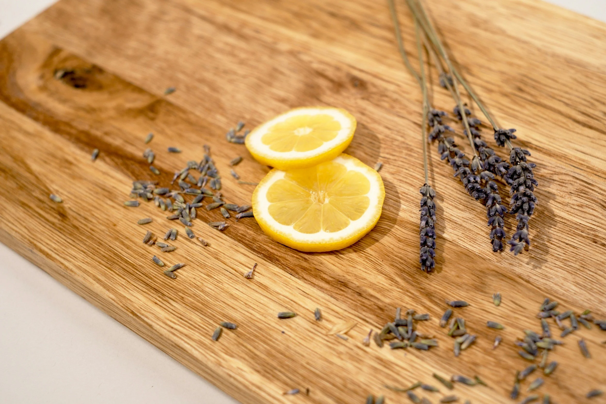 Two lemon slices, dried lavender sprigs, and scattered lavender buds on a wooden cutting board.