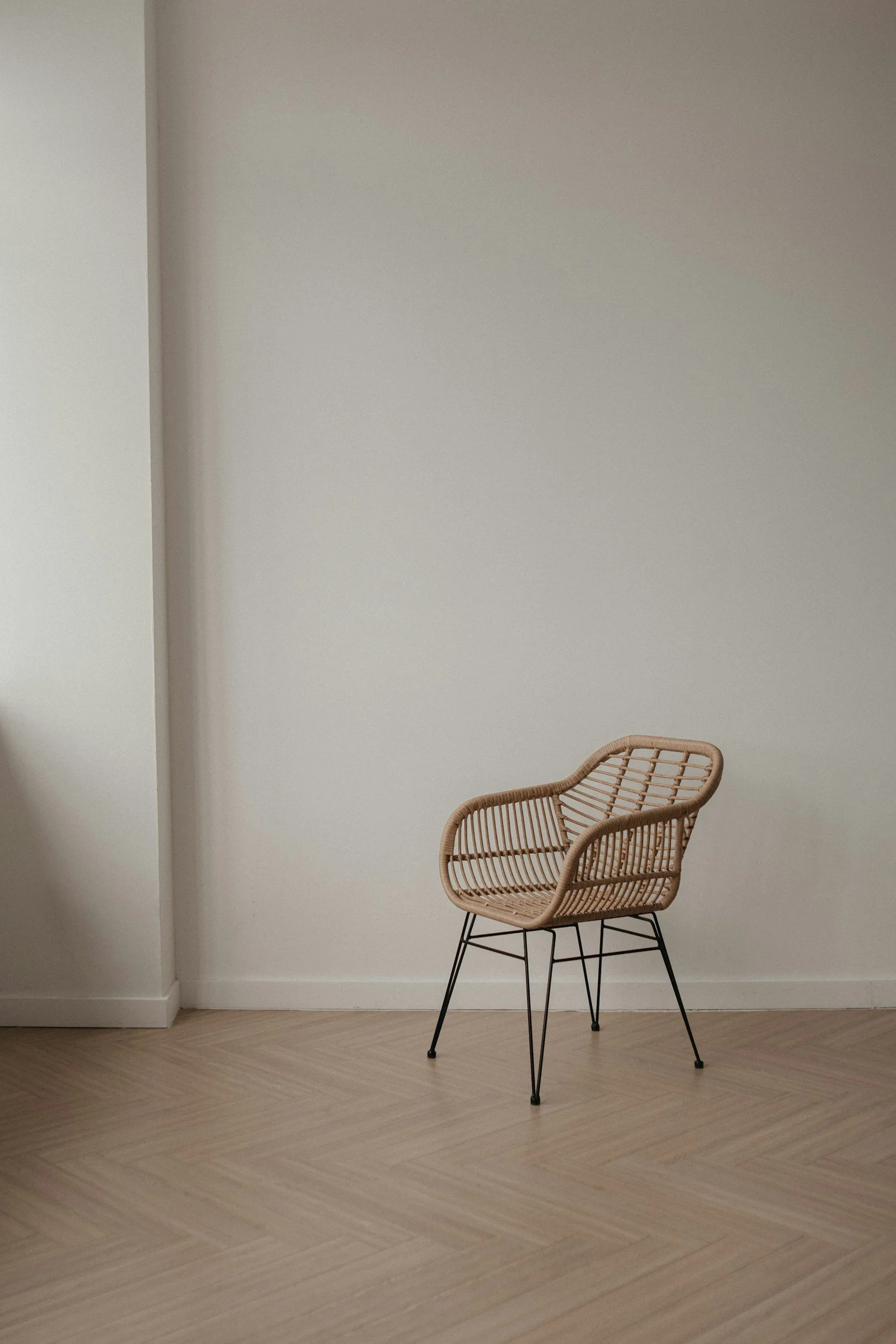 A modern wicker chair with black metal legs in a room with beige flooring and white walls.