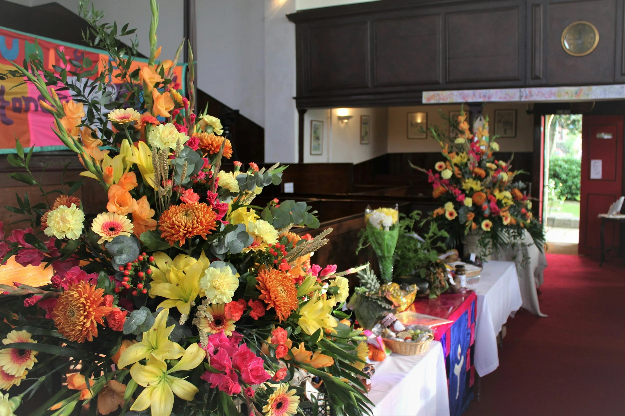 Colorful flower arrangements on a table inside a building, with a dark wood wall and a red door in the background.