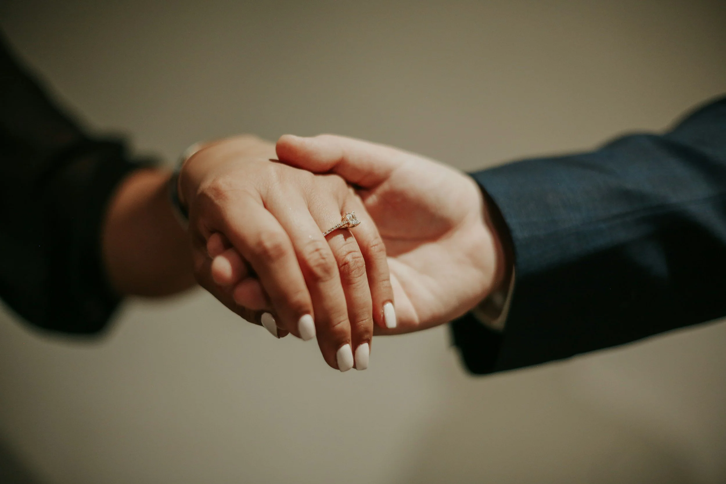 Close-up of a man and woman holding hands, with the woman displaying a diamond engagement ring on her finger.
