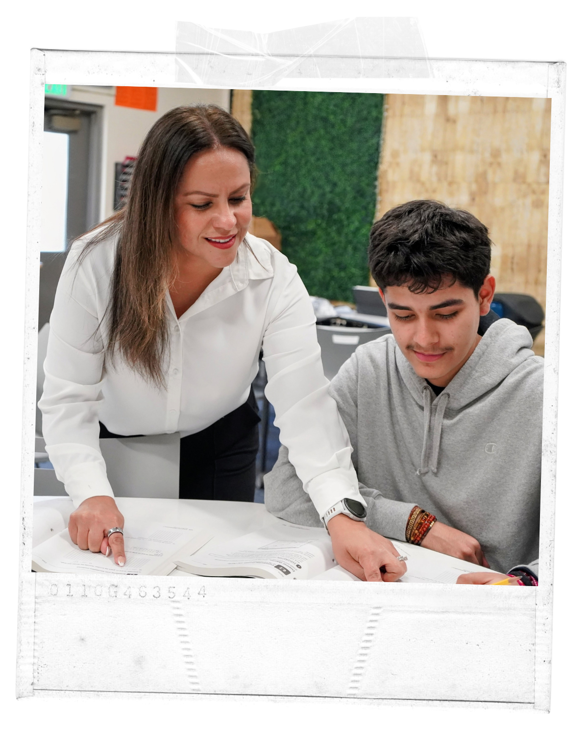A woman teaching a young man at a table with open textbooks in a classroom setting.