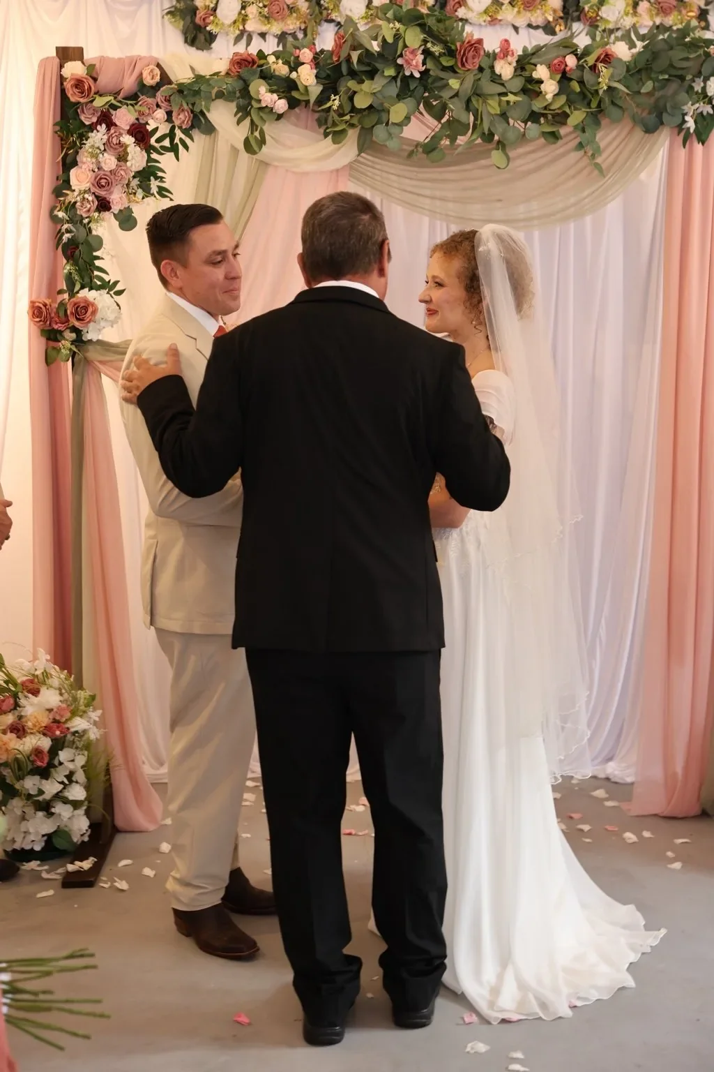 A couple exchanges vows beneath a floral arch with blush and ivory draping.