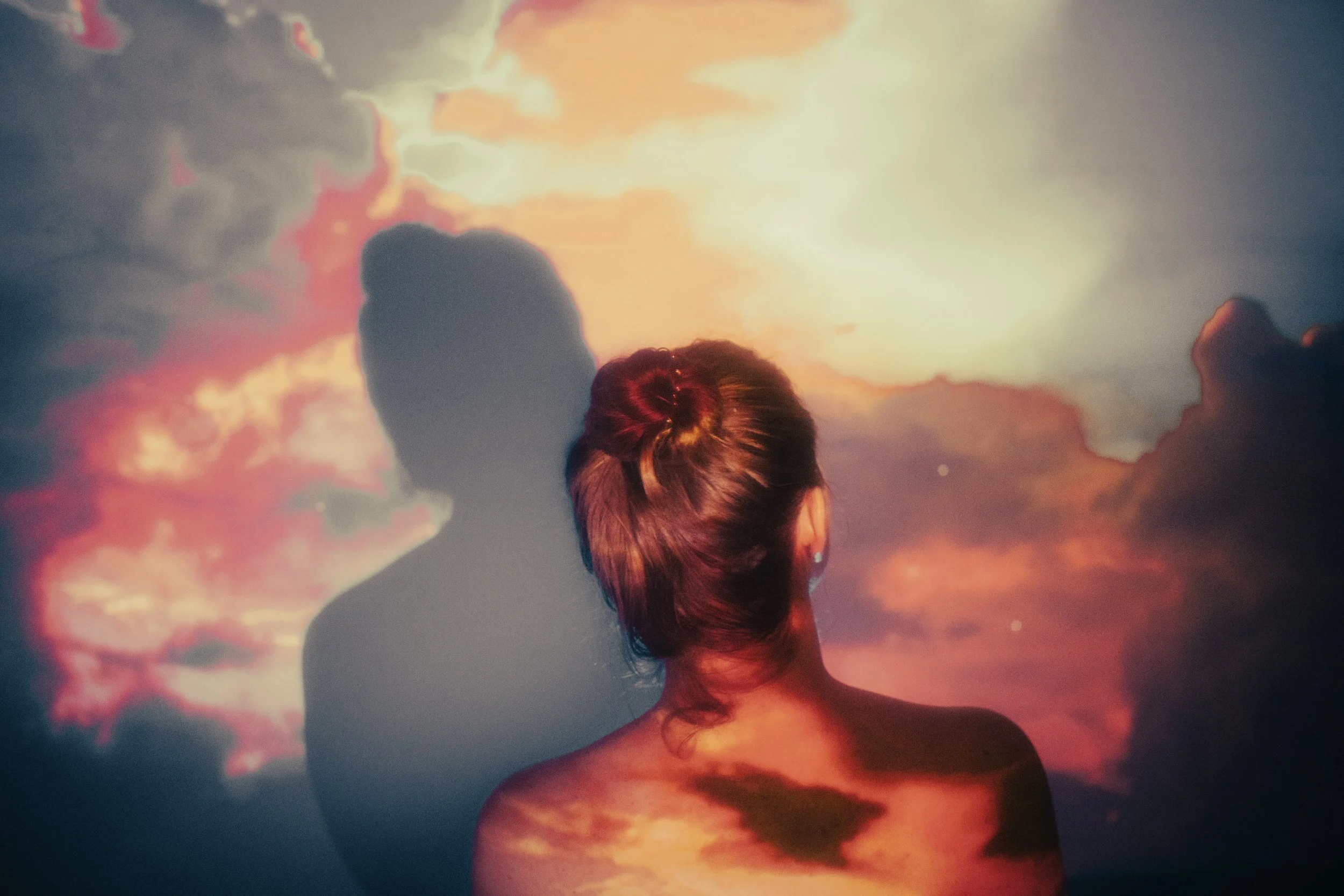 Sunset sky image projected onto a person's back and the wall in front of them, their shadow visible on the wall