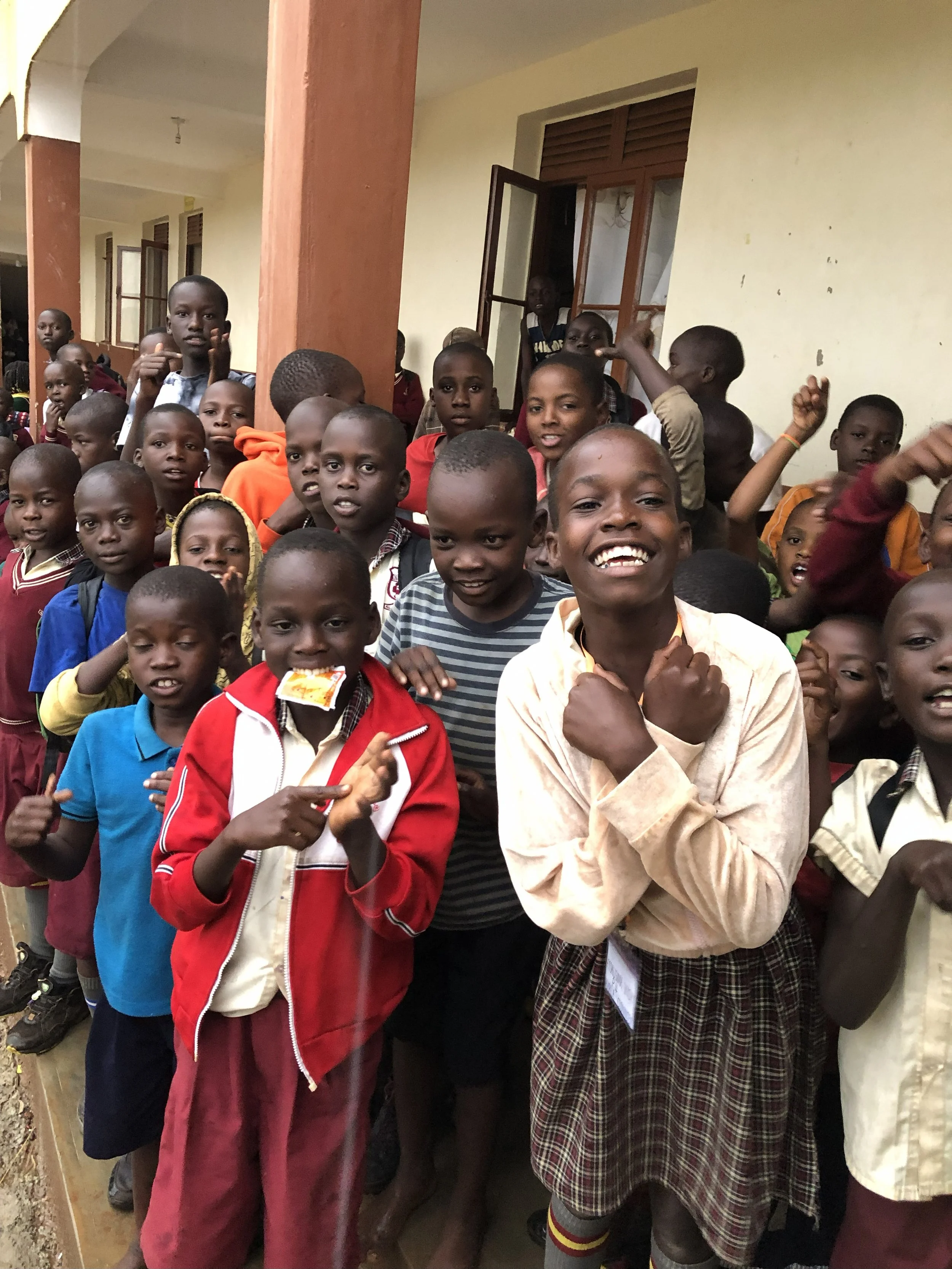 Group of children, some smiling and some serious, standing outside a building with open windows and brown pillars.