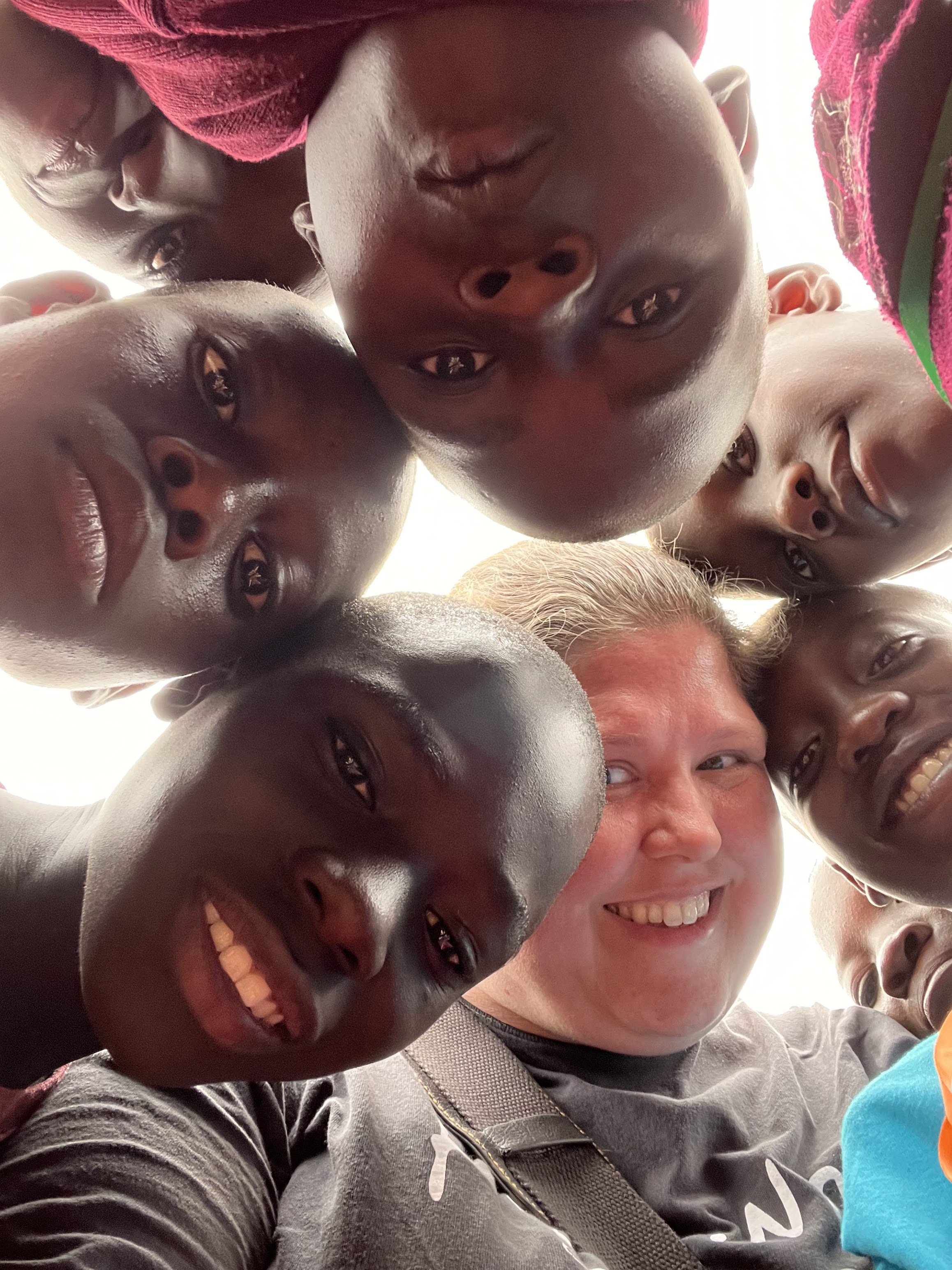 Group of smiling children and a woman looking down into the camera.