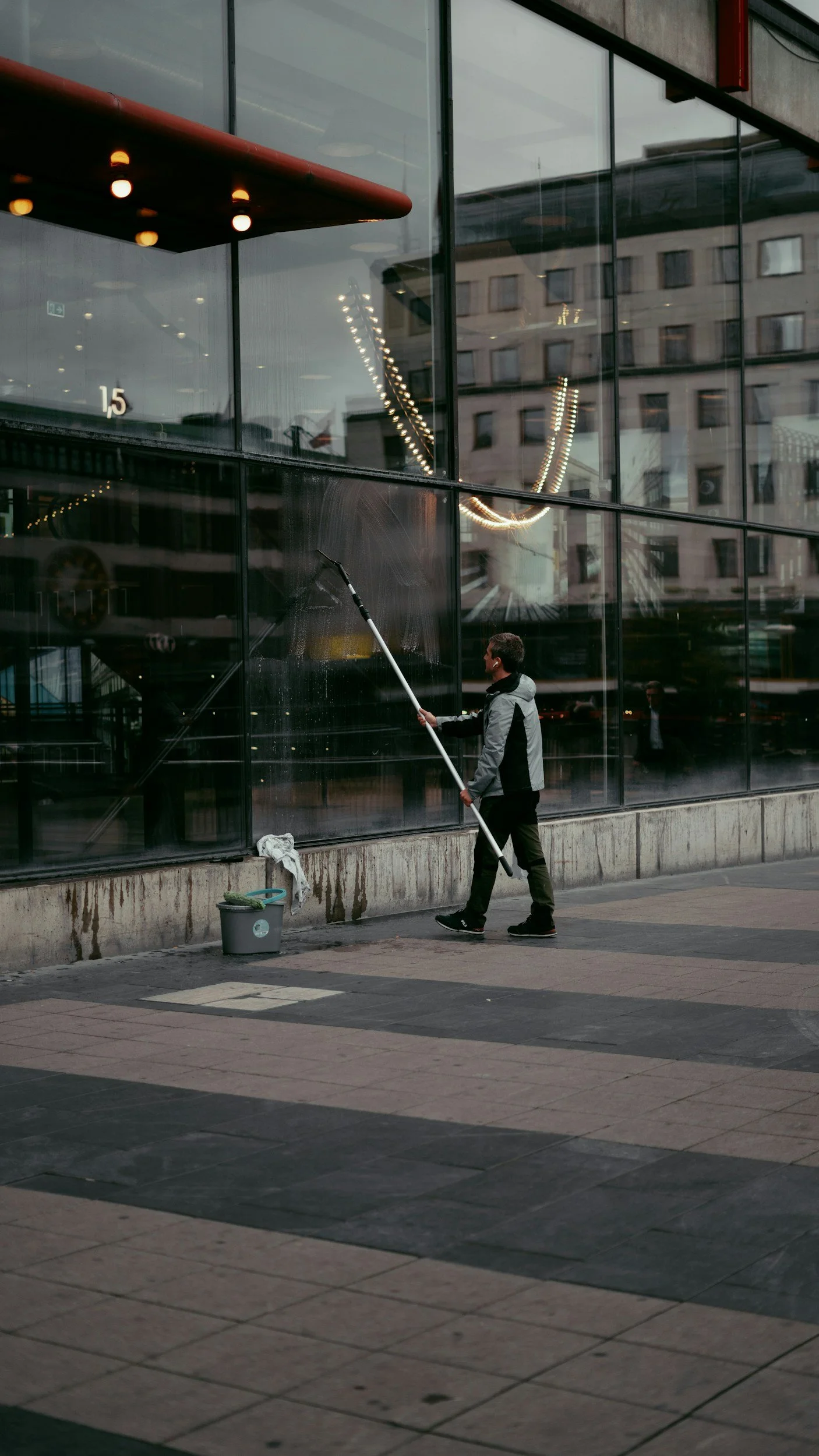 A man cleaning the glass window of a building with a long-handled squeegee outside during daytime