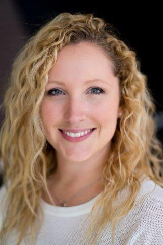 Close-up of a smiling woman with curly blonde hair wearing a white shirt.