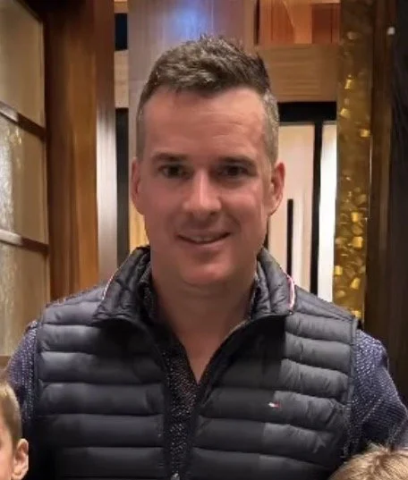 A woman with short curly hair and glasses smiling in an indoor setting.